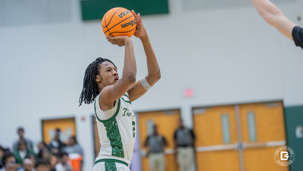 Jervaz'e Salley rises for a jump shot in Woodland High’s white and green uniform as a defender contests from the right, gym doors and crowd blurred behind him.