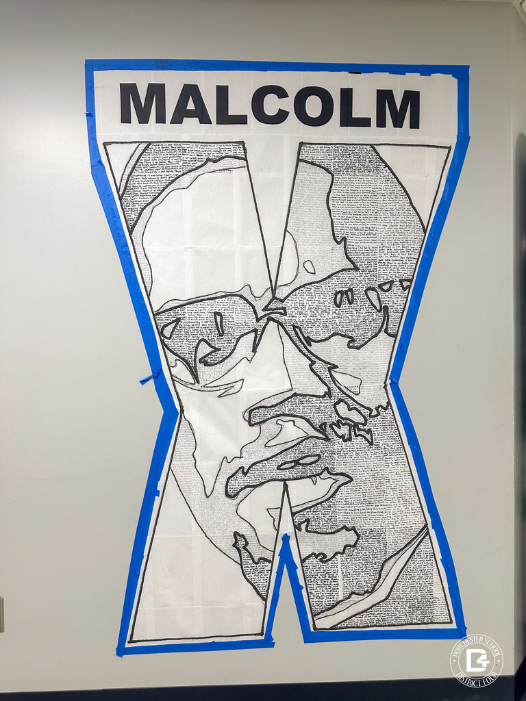 Large black and white mural shaped like the letter X with the name “MALCOLM” at the top. The inside of the X forms a detailed portrait of Malcolm X made from handwritten text, outlined in black and bordered in blue.