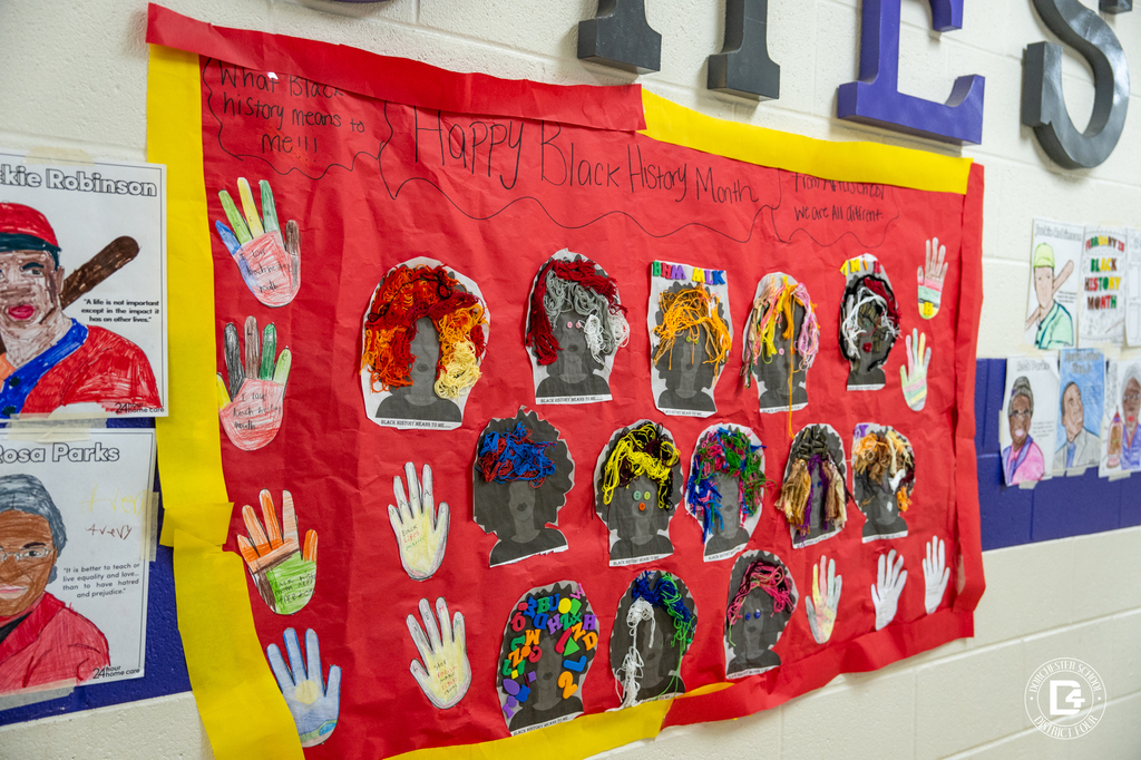 A large red and yellow bulletin board titled “Happy Black History Month” features student silhouette art with yarn hair, decorated hand cutouts, and written reflections about what Black history means to them.