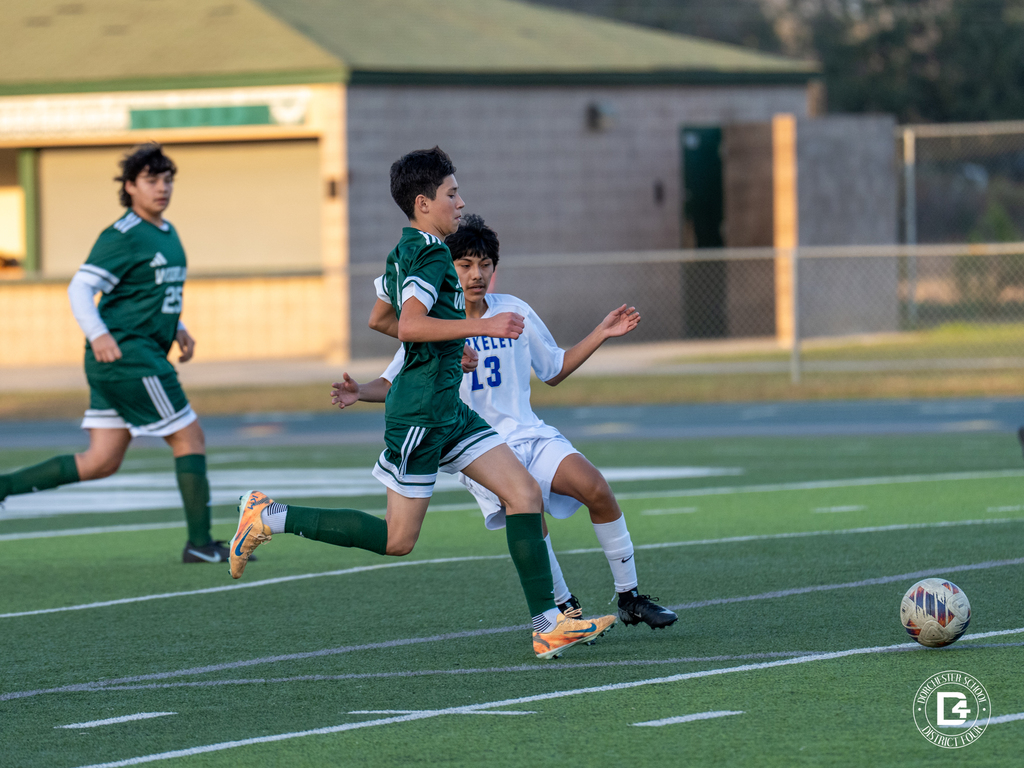 A Woodland boys soccer player in a green uniform dribbles the ball while a defender from the opposing team moves in to challenge.
