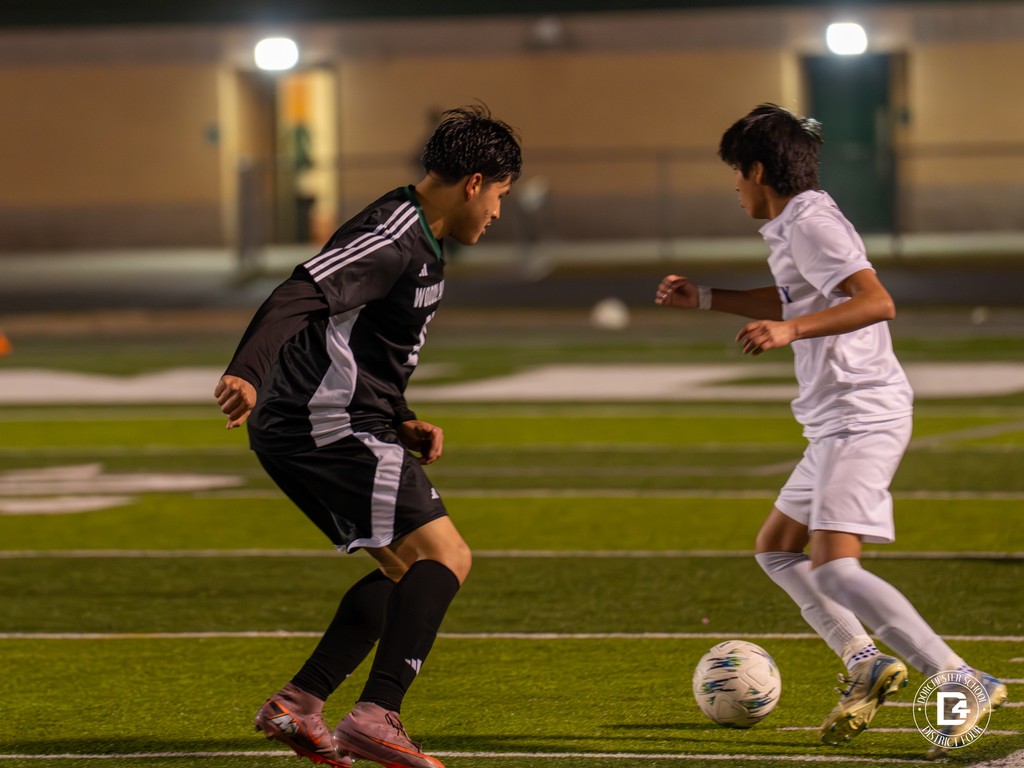 Two soccer players from opposing teams face off for control of the ball during a night match on the turf field.