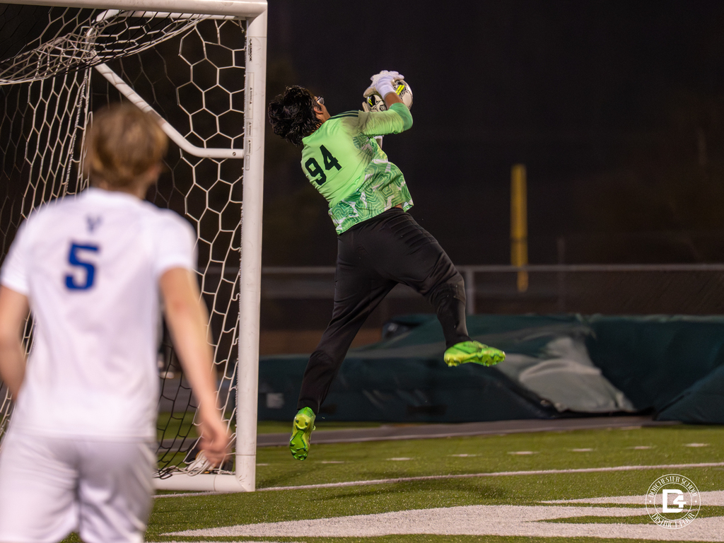 A Woodland goalkeeper wearing number 94 leaps into the air to make a save near the goal during a night soccer game.