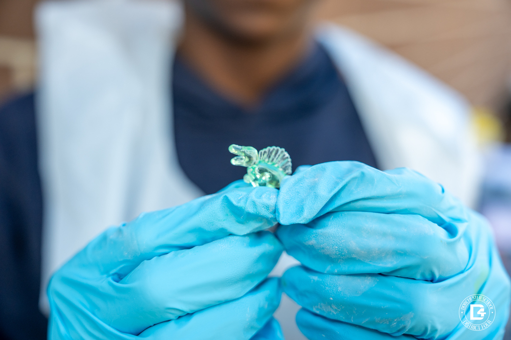 Close-up of a small plastic dinosaur fossil being held with blue gloves during the hands-on fossil discovery activity.