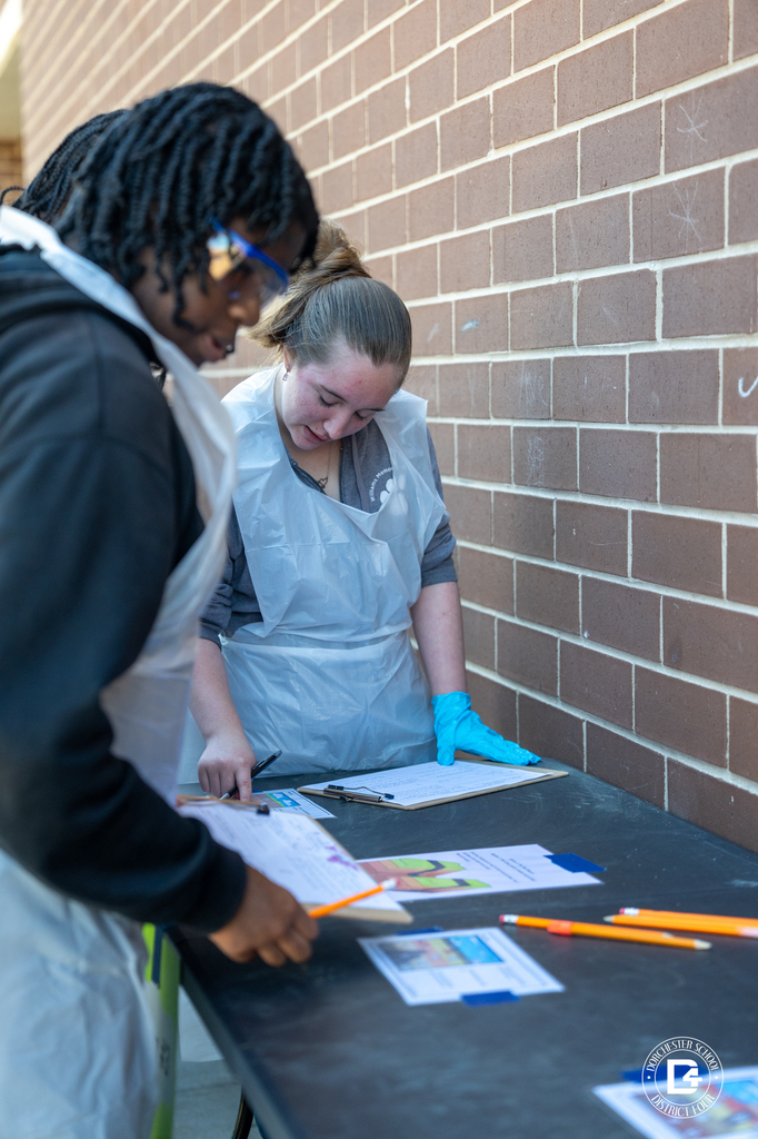 Two students review instructions and record findings on a clipboard while participating in the Dino Dig Day fossil investigation activity.