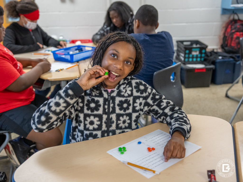 Student smiles and eats an M&M while working on the probability activity at a classroom table.