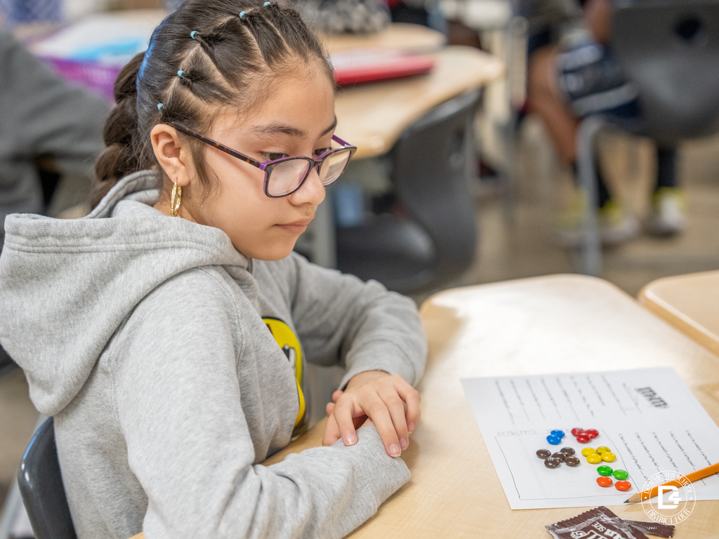 Student wearing glasses studies a worksheet with M&M’s sorted by color during a hands-on math lesson.