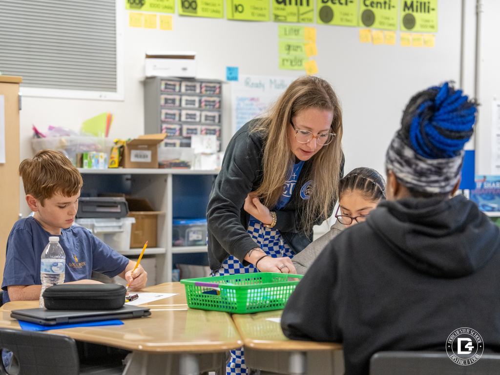 Mrs. Pafford leans over a table helping students as they complete a hands-on probability activity using M&M’s.