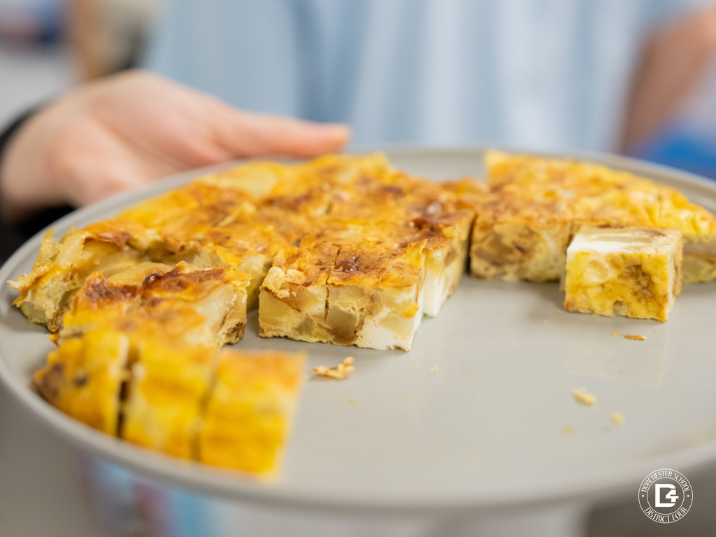 Close-up of a plate of traditional food cut into small squares, prepared for students to sample as part of the cultural presentation.