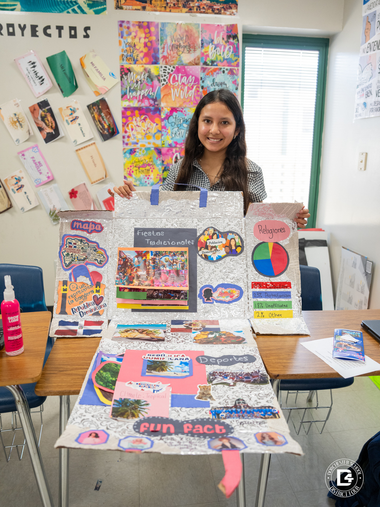Student stands behind a presentation board about the Dominican Republic featuring maps, food, traditions, and cultural facts during a Spanish class cultural project at Woodland High School.