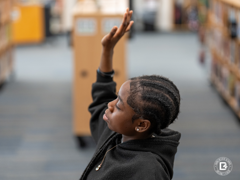 Student raises her hand to respond to a question during the leadership activity in the library.
