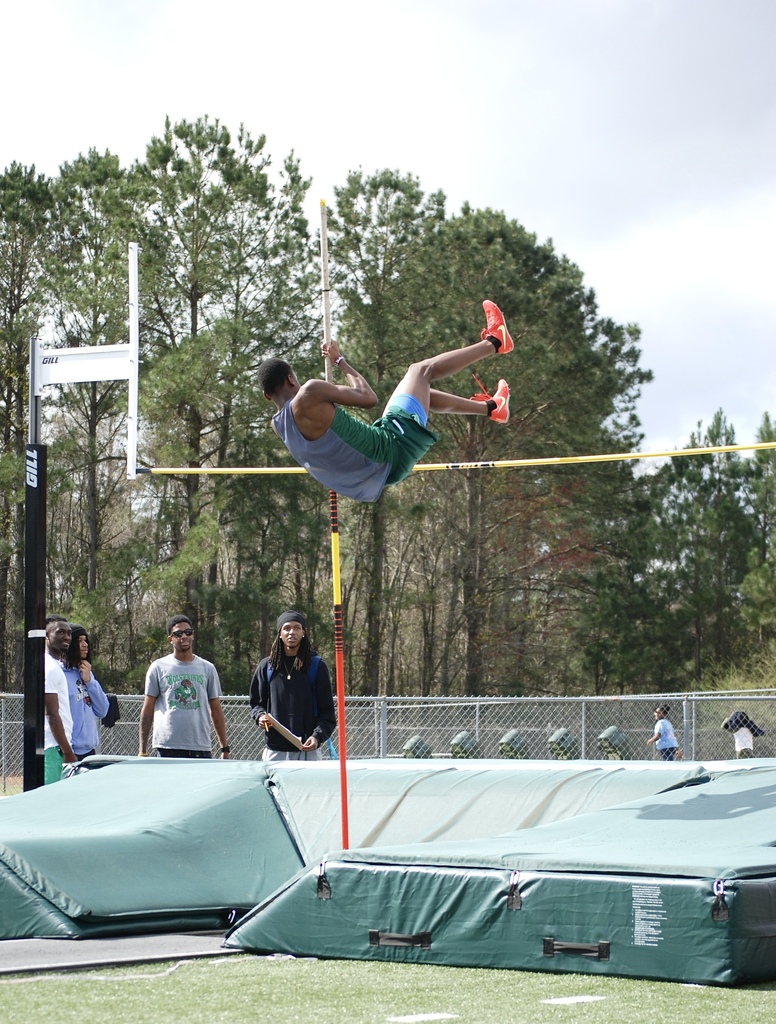 Woodland High School pole vaulter clears the bar while landing toward the mat during competition.