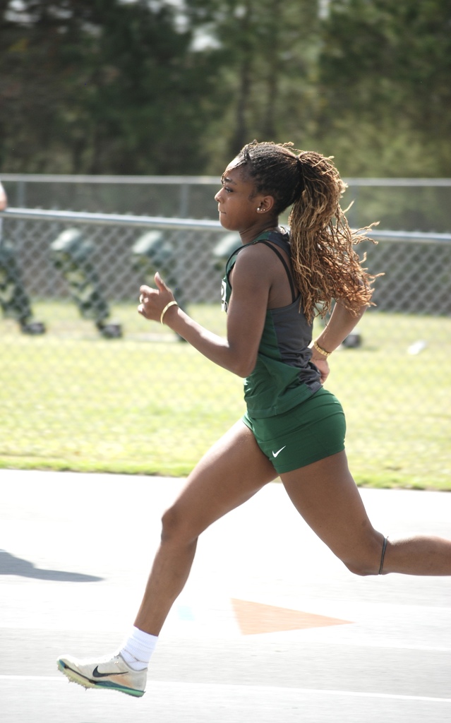 Woodland High School runner sprints down the track during a race as spectators watch from the stands.