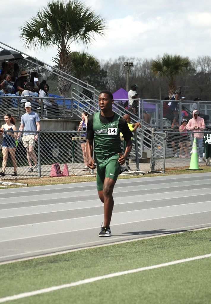 Woodland High School runner sprints down the track during a race as spectators watch from the stands.