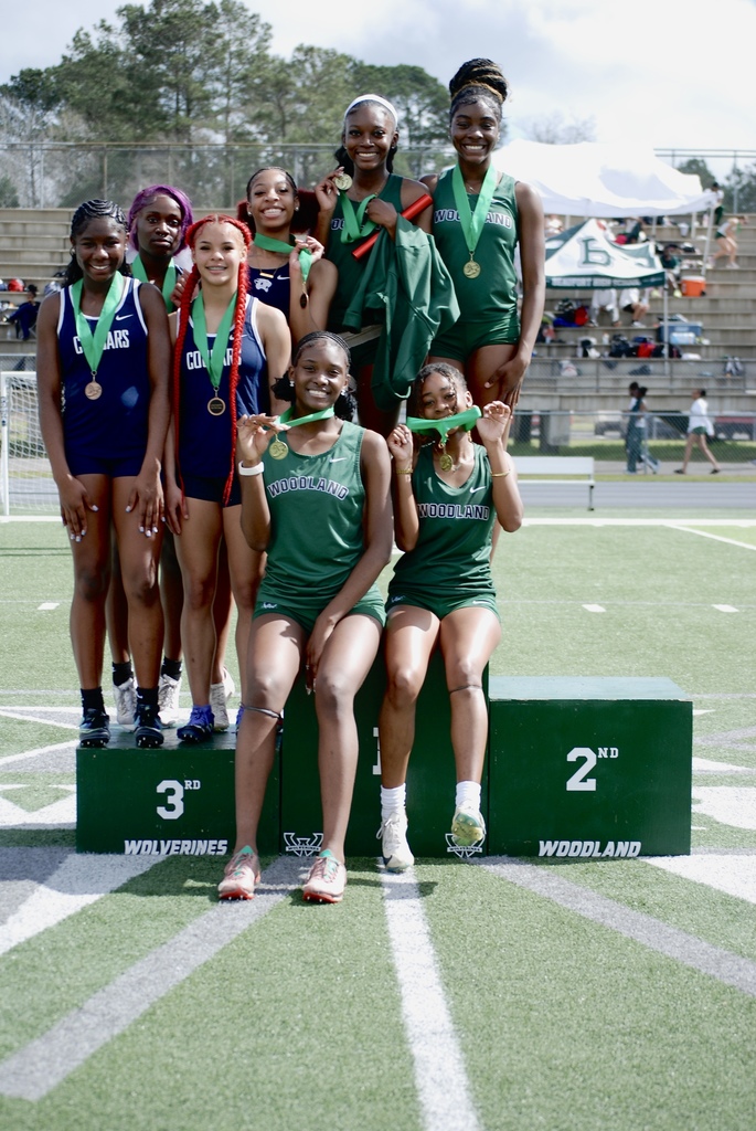 Woodland High School girls track athletes pose together on the podium with medals after competing in events at the track meet.
