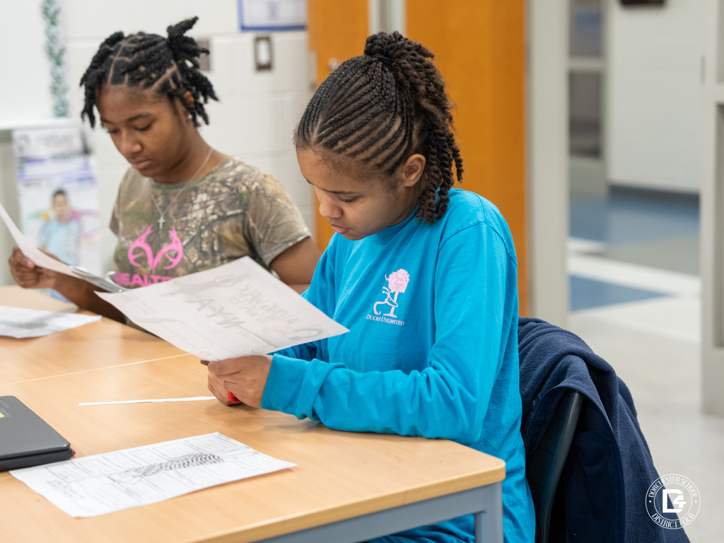 Students sit at a table reading and reviewing their printed character analysis pages during the activity.
