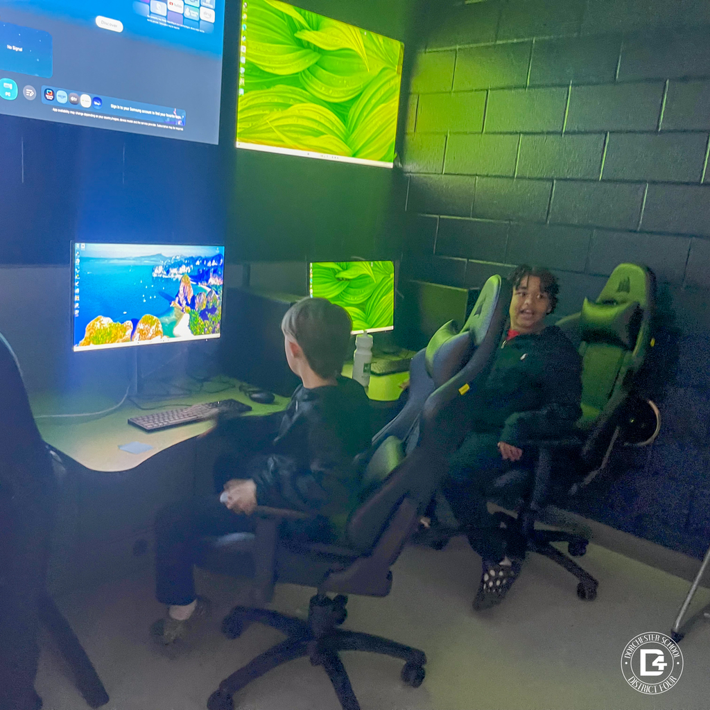 Two students sit in a technology lab at Woodland Middle School, using desktop computers with multiple monitors mounted on the wall, as they explore digital tools during the Rising 6th Grade Parent Open House.