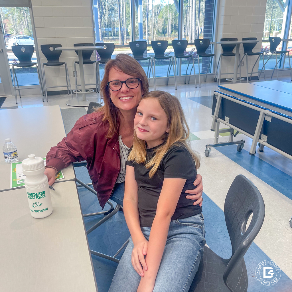 A parent and child sit together at a table, smiling and embracing during the event, with Woodland Middle School materials visible nearby.