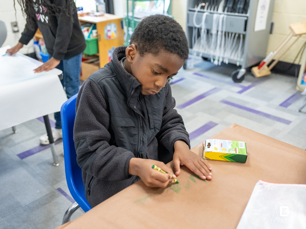 Student sitting at a desk focused on coloring with a green crayon during the ecosystem activity.