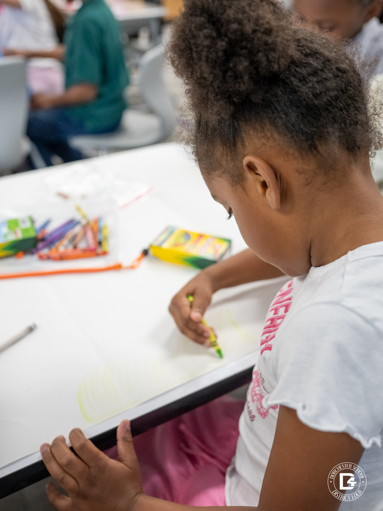 Student seated at a desk concentrating while drawing with a crayon on paper.