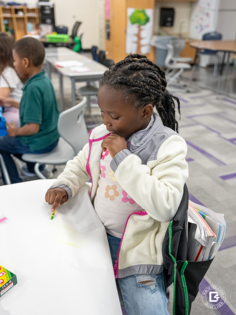 Student coloring on white paper with crayons during a classroom activity.