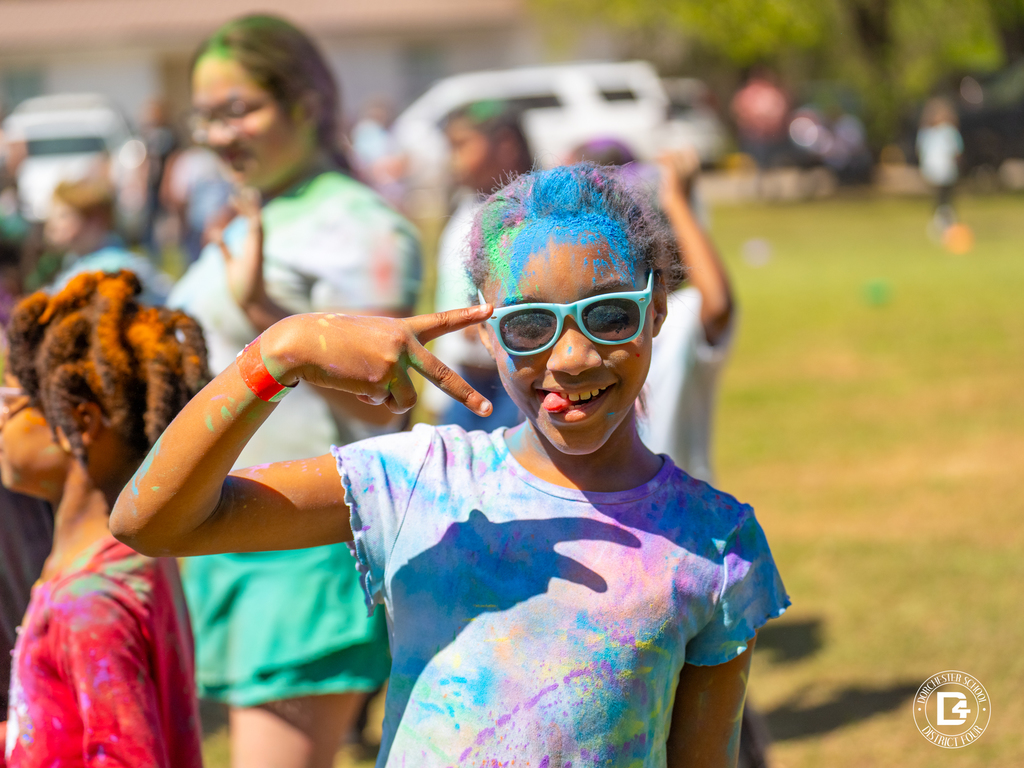 Student smiling and posing with peace signs, wearing sunglasses and covered in bright color powder during the Clay Hill Elementary Color Fun Run.