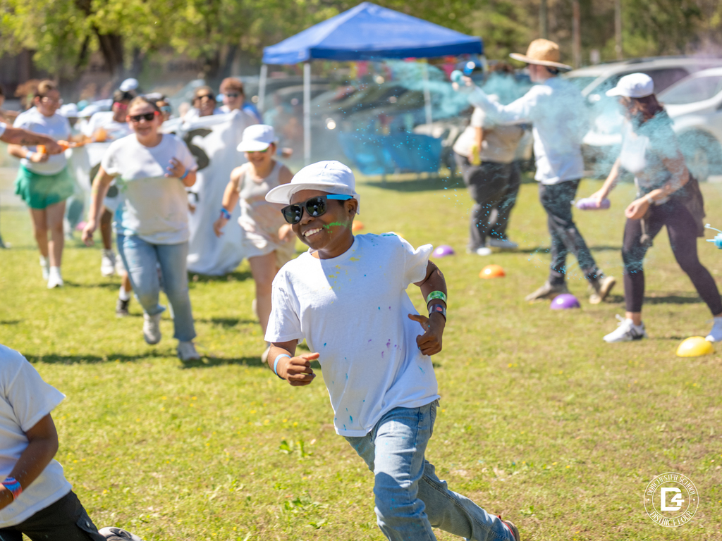 Group of students running across the field as color powder is tossed in the air behind them during the Clay Hill Elementary Color Fun Run.