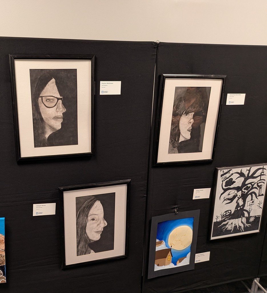 Student artwork displayed on black exhibition panels, featuring charcoal portrait drawings by Payton Matthews, Abigail Meree, and Samantha Reinmiller, alongside a nighttime moonlit scene by Kamar Pringle and a black and white silhouette illustration.