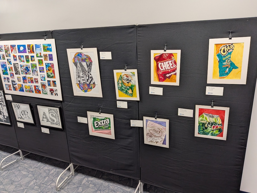 Student artwork displayed on black exhibition panels at Charleston Southern University, including colorful drawings of snack foods such as Cheez-Its, Goldfish crackers, Extra gum, and a Mountain Dew can, along with illustrated and typographic pieces.