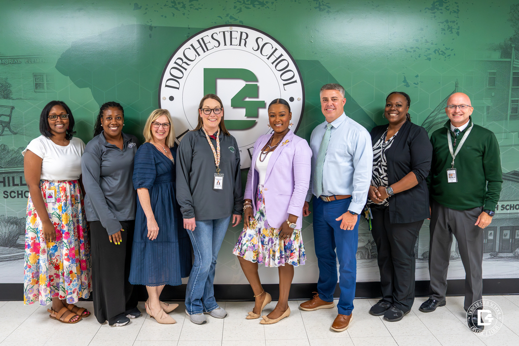 A group of Dorchester School District Four leaders and assistant principals stand together in front of a green district-branded background with the district seal behind them.
