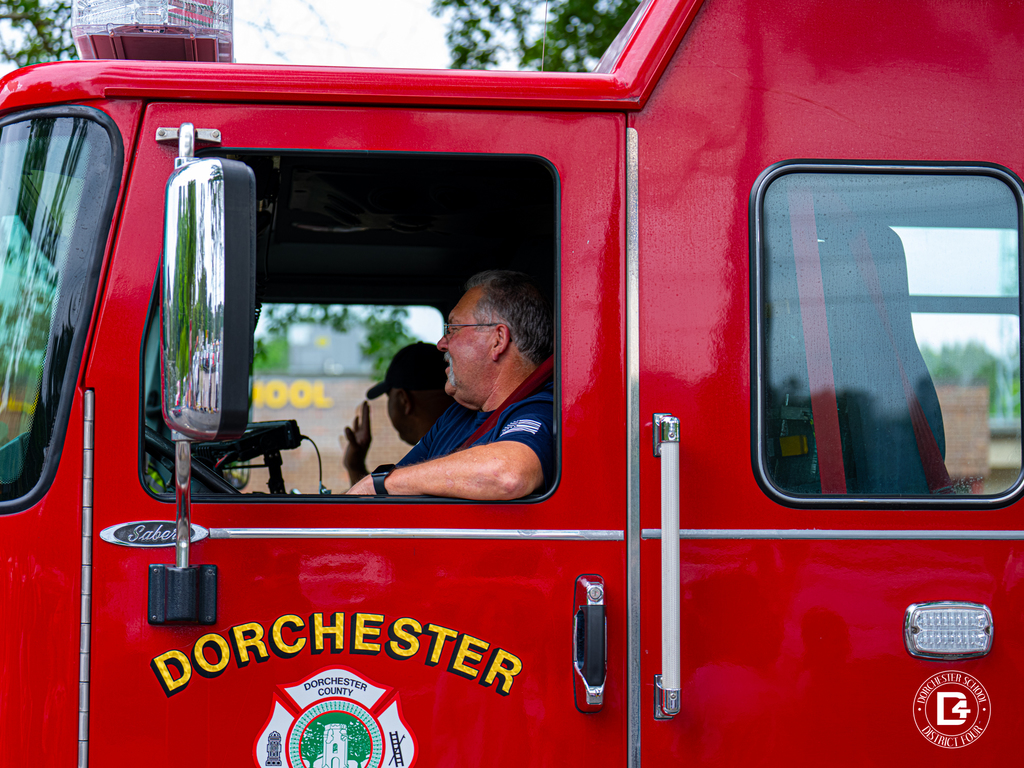 A red Dorchester County fire truck passes by with firefighters visible inside the cab during the school parade.