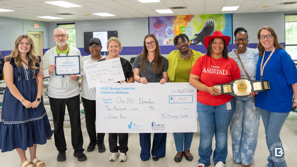 Clay Hill Elementary School staff members, wellness team, musc reps and district staff pose together holding a $2,000 award check, certificate, and championship wellness belt during a school celebration event.
