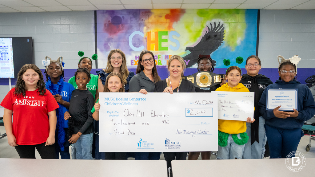 Clay Hill Elementary students, staff, and MUSC reps gather together holding a $2,000 MUSC Boeing Center for Children’s Wellness award check, certificate, and wellness championship belt in the school cafeteria.