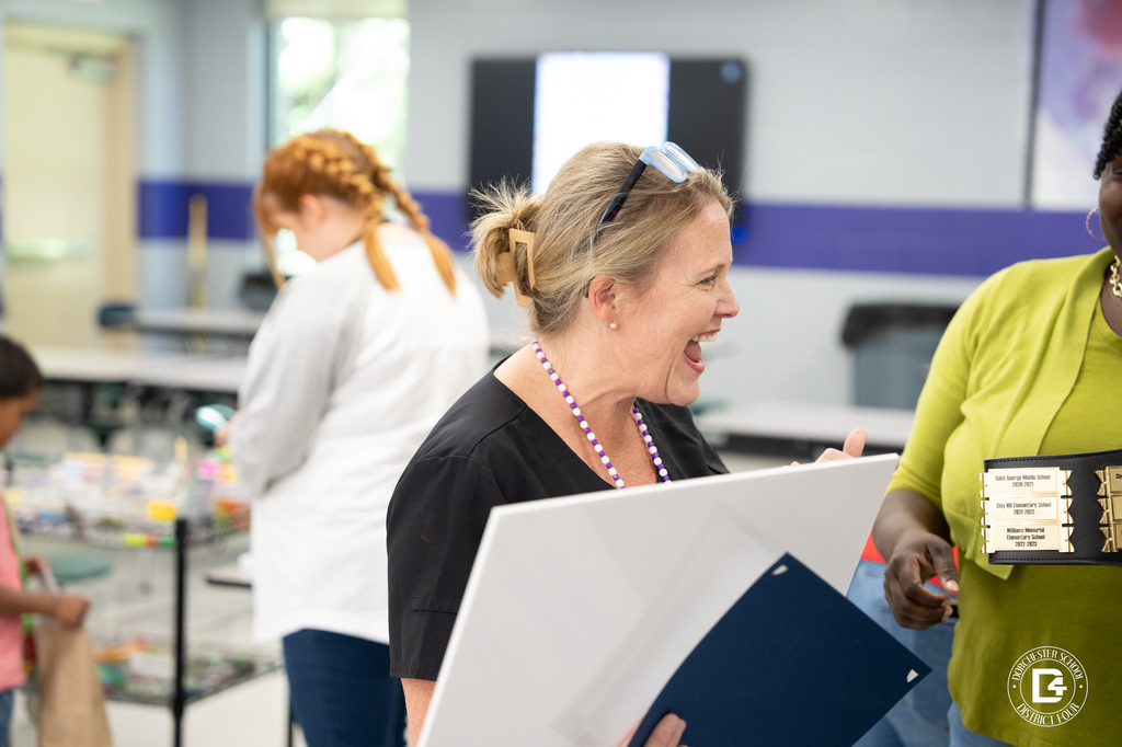 Nurse Weathers smiles and talks with another staff member while holding award materials during the Clay Hill Elementary wellness celebration event.