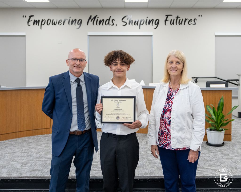 Ethan Dibello stands between two district representatives while holding his South Carolina Junior Scholar Award of Merit certificate during the May 19 DD4 Board Meeting.