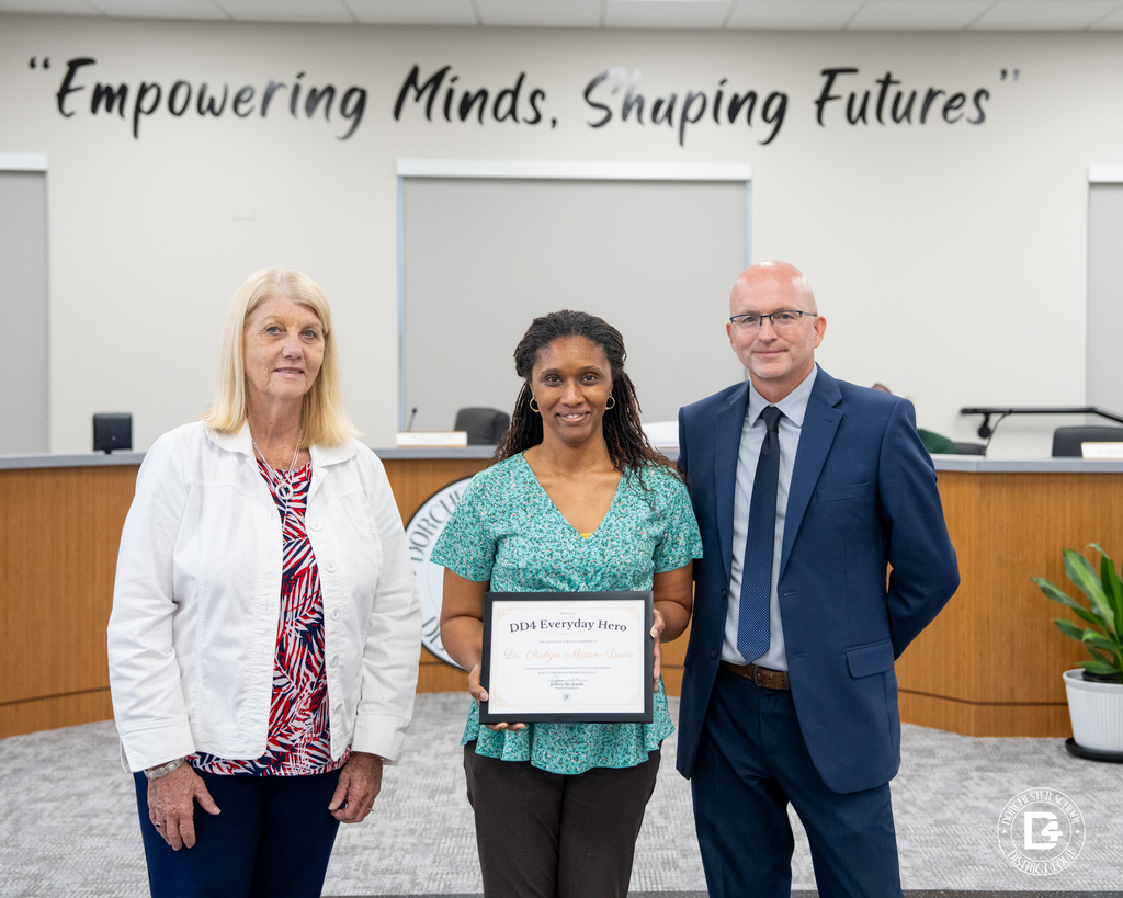 Dr. Robyn Mixon-Davis stands between two district representatives while holding her DD4 Everyday Hero award during the May 19 Board Meeting.