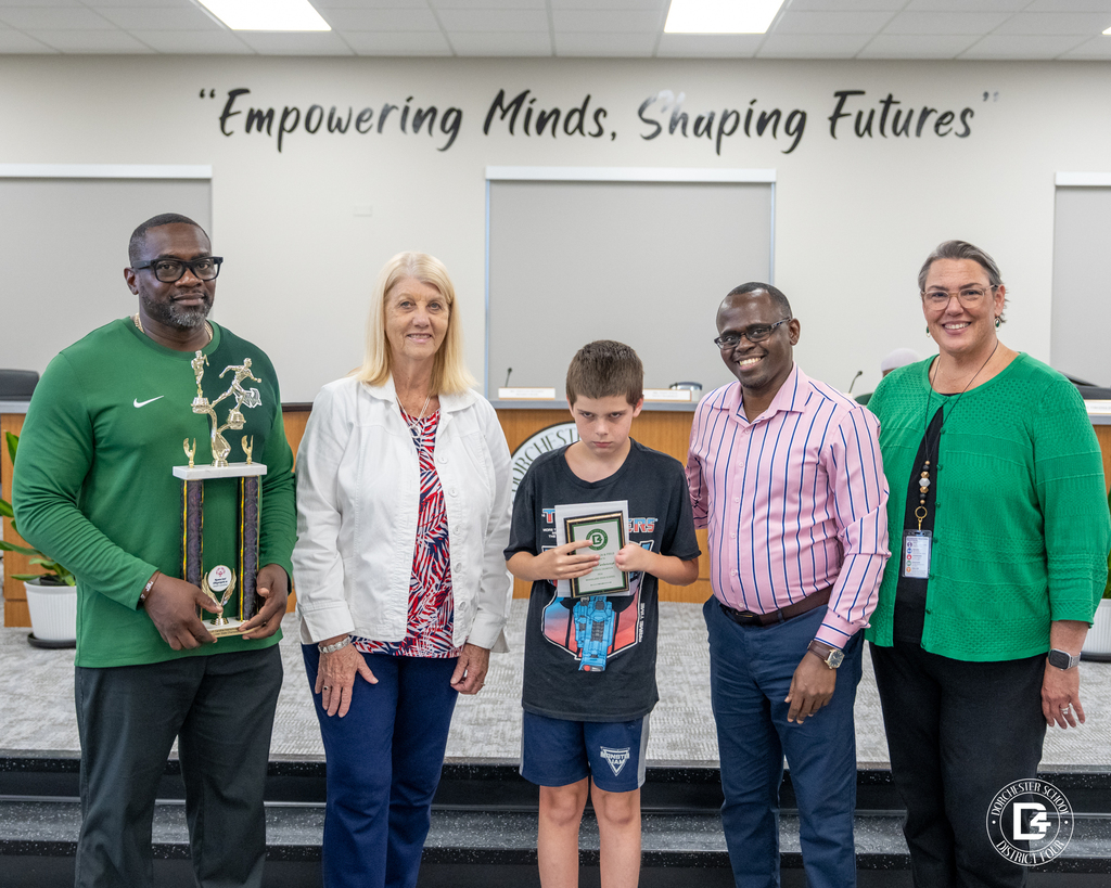 A Unified Track & Field student athlete stands with coaches and district representatives while holding an award during the May 19 DD4 Board Meeting.