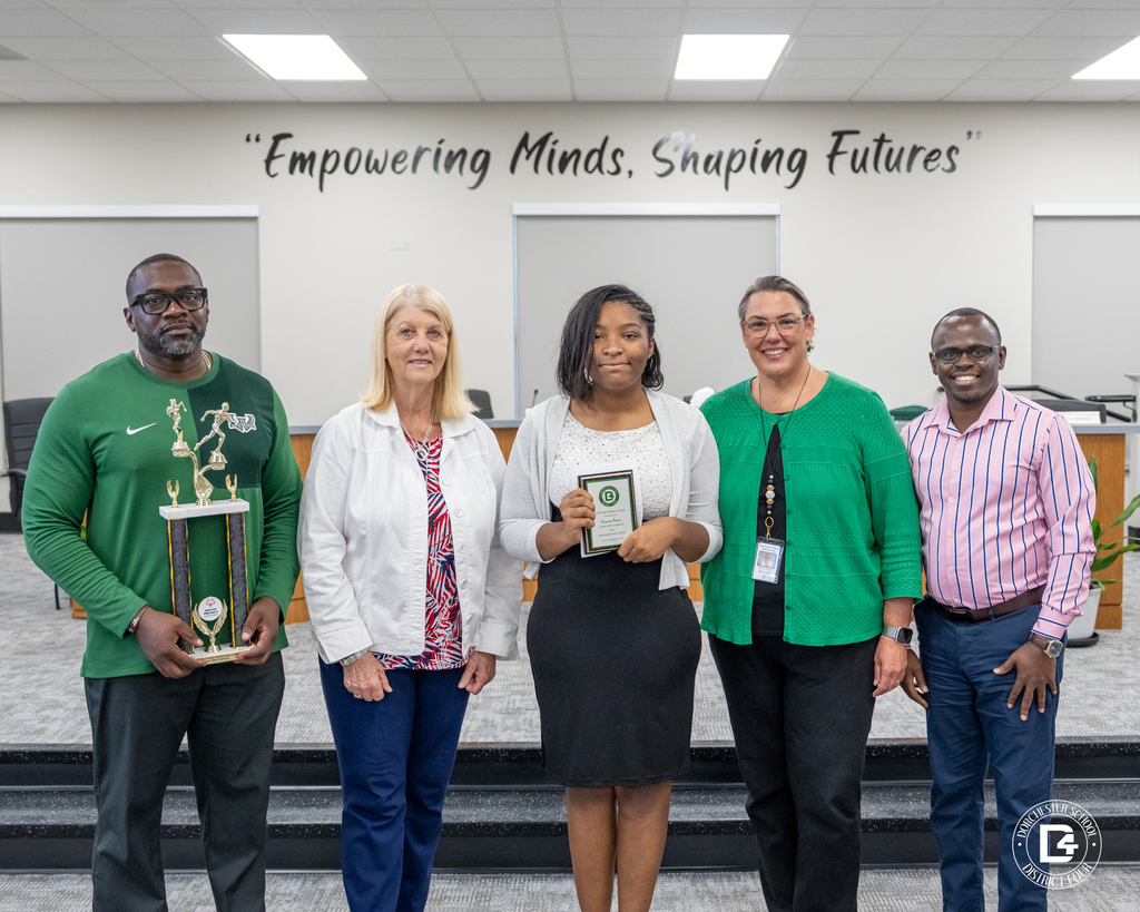 A Unified Track & Field student athlete stands with coaches and district representatives while holding an award during the May 19 DD4 Board Meeting.