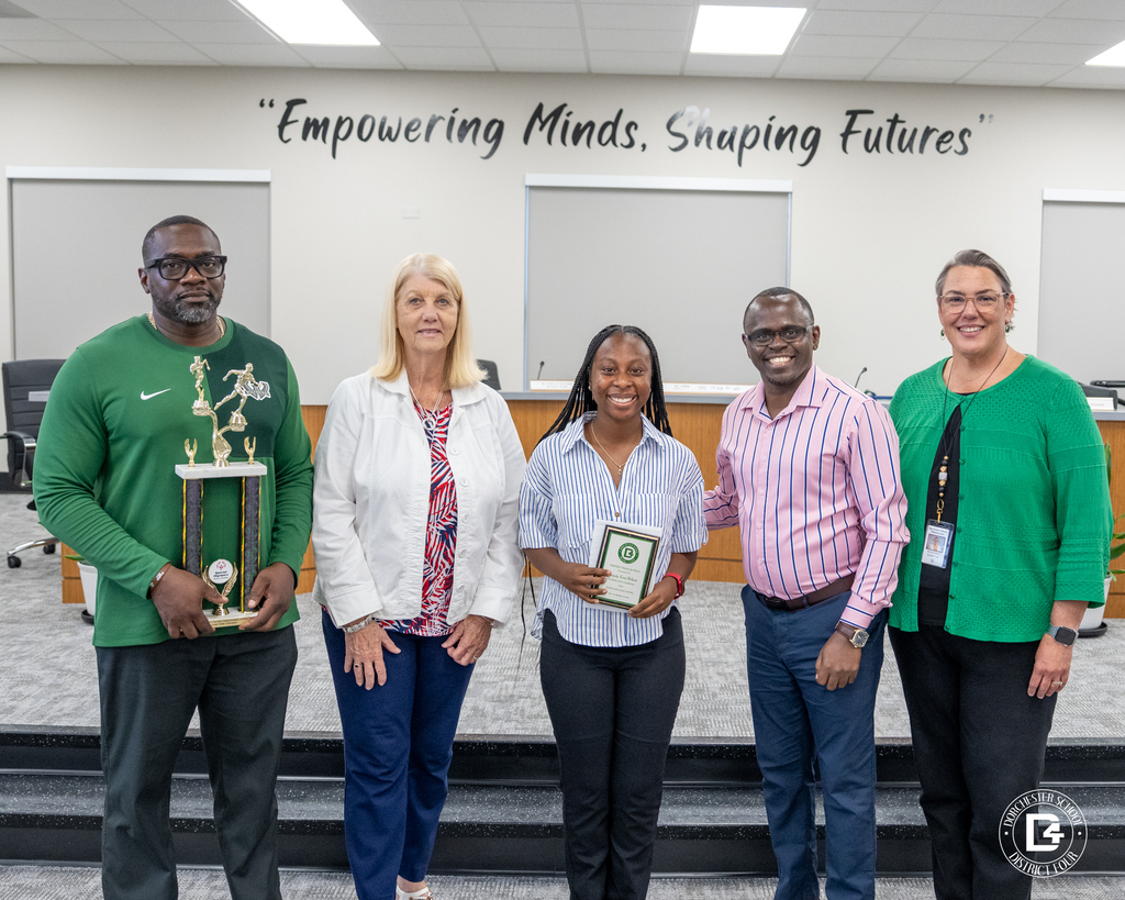 A Unified Track & Field student athlete stands with coaches and district representatives while holding an award during the May 19 DD4 Board Meeting.
