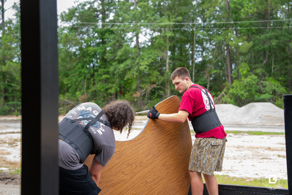 Students move a large tabletop while wearing lifting belts during summer school preparations.