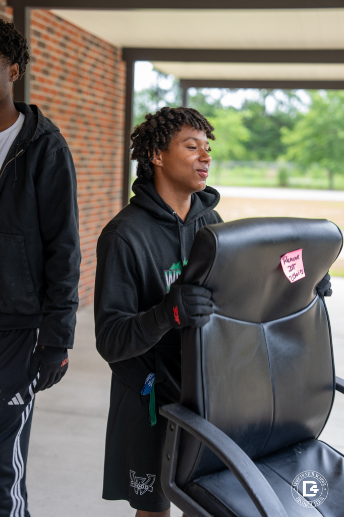 Student carries an office chair to help prepare a school building for the new year.
