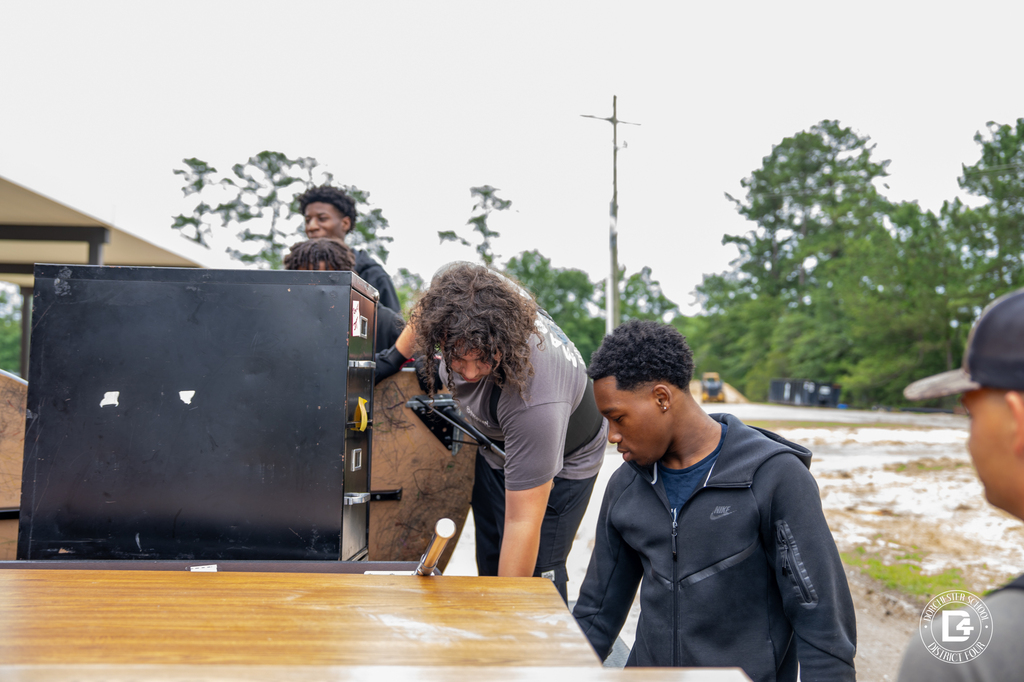 Summer student workers load office furniture onto a trailer outside a school building.