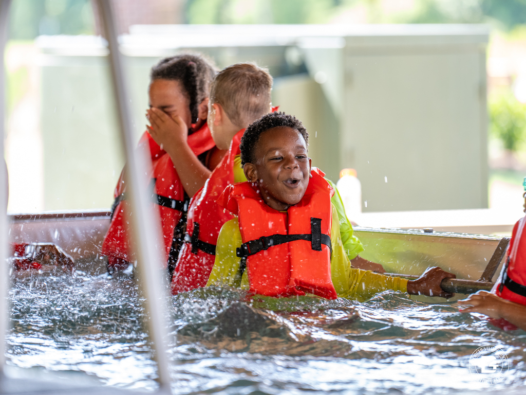 Students wearing life jackets participate in a hands on water safety lesson under instructor supervision