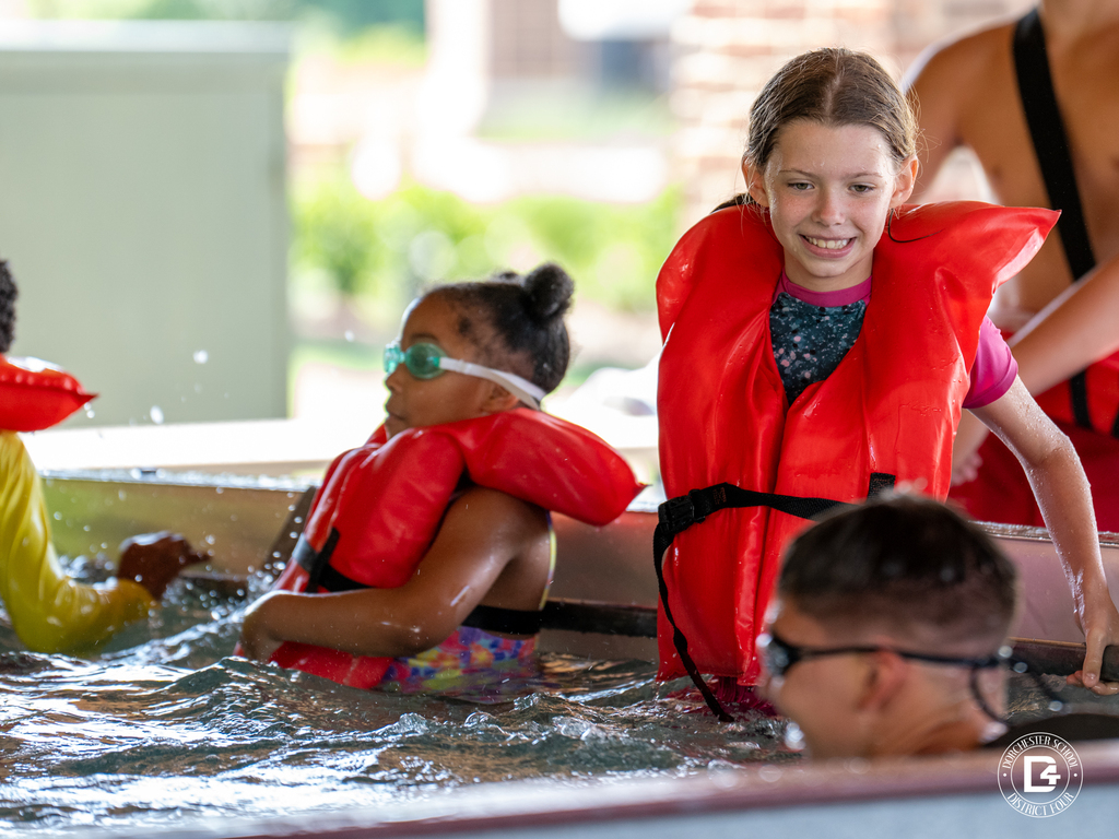 Students wearing life jackets participate in a hands on water safety lesson under instructor supervision
