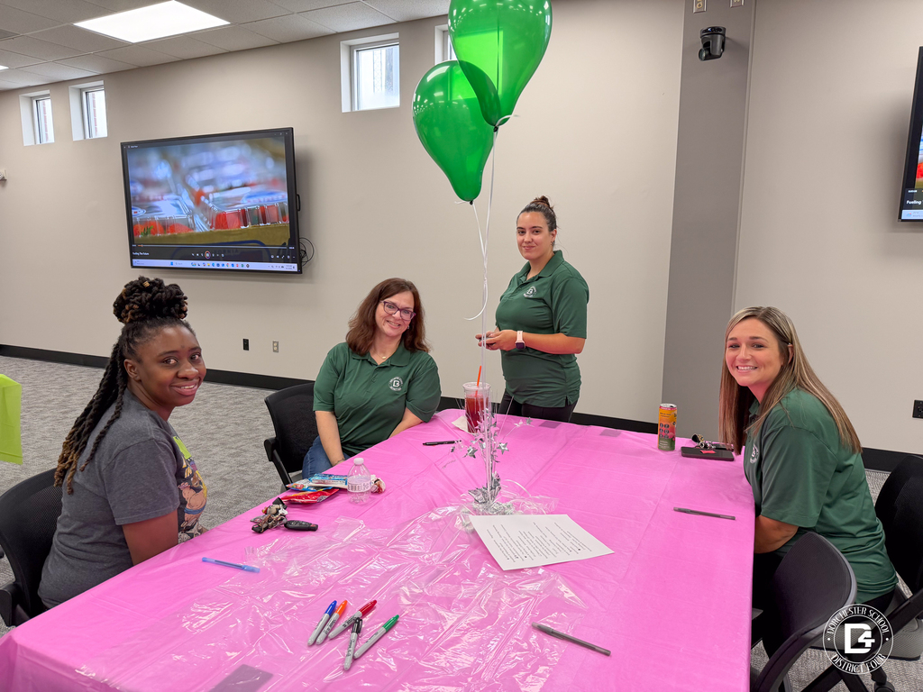 Four DD4 Food Services employees smile around a pink table decorated with green and white balloons during the district's Food Services in-service.