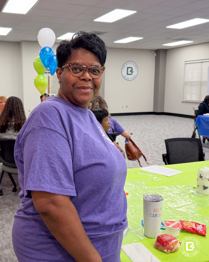 A DD4 Food Services employee smiles while standing beside a decorated table during the district's Food Services in-service.