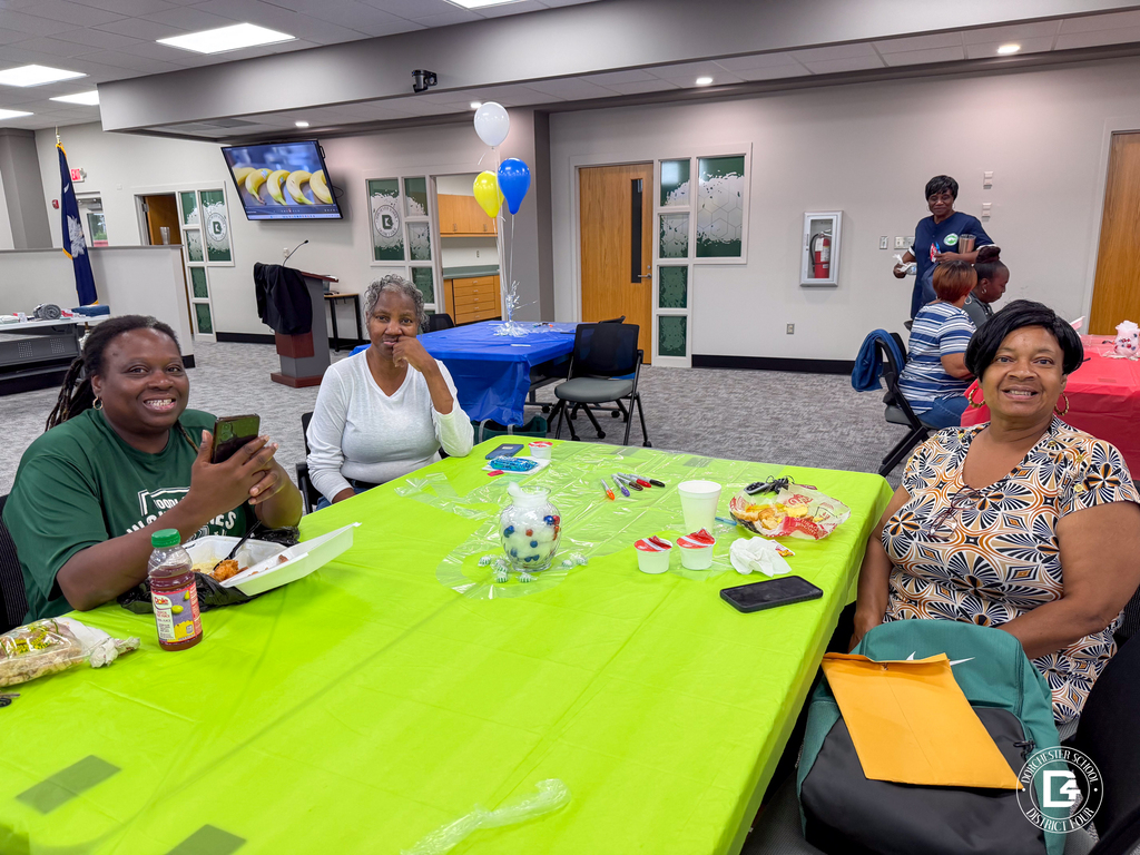 Three DD4 Food Services staff members smile around a green table during the district's Food Services in-service.