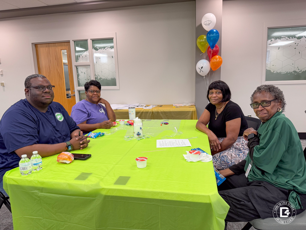 Four DD4 Food Services staff members gather around a green table, smiling during the district's Food Services in-service.