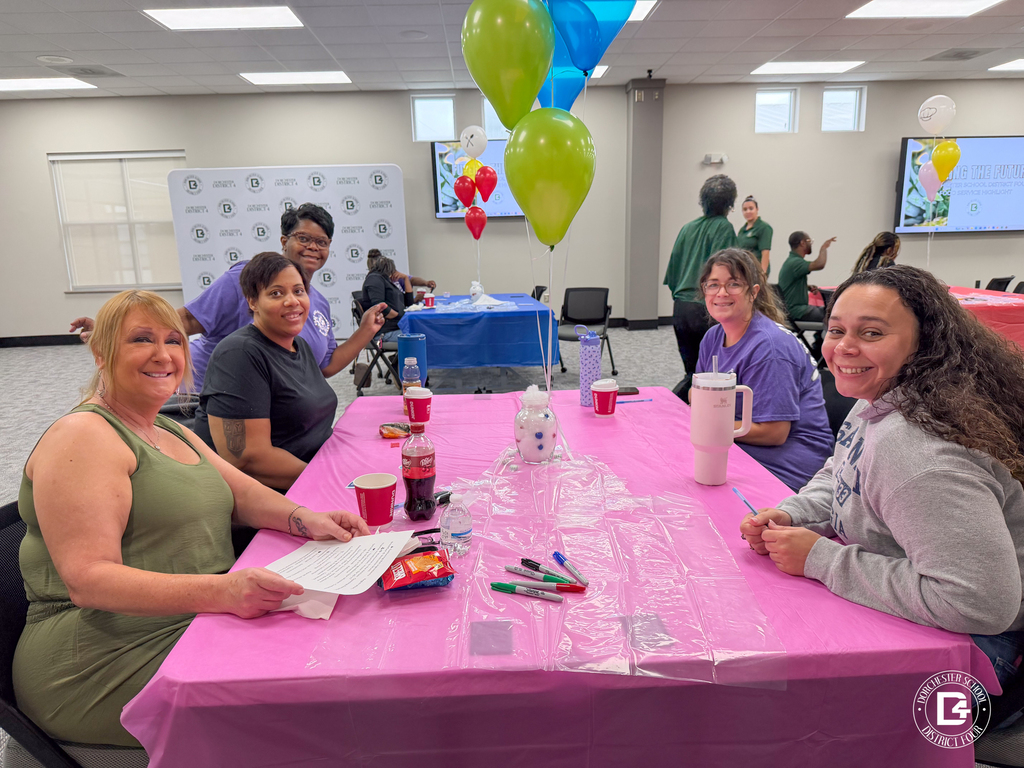 Five DD4 Food Services staff members smile around a pink table decorated with balloons during the district's Food Services in-service.