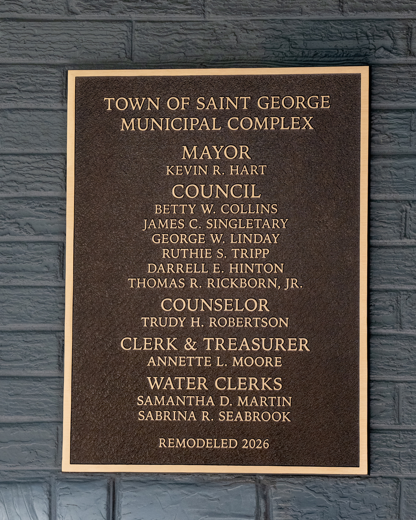 A bronze plaque mounted on a gray brick wall reading "Town of Saint George Municipal Complex," listing Mayor Kevin R. Hart, the Town Council members, Counselor, Clerk & Treasurer, and Water Clerks, with "Remodeled 2026" at the bottom.