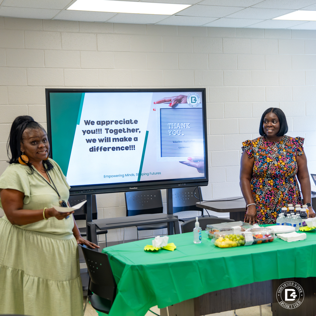 Two women stand beside a presentation screen during the mentoring program orientation.